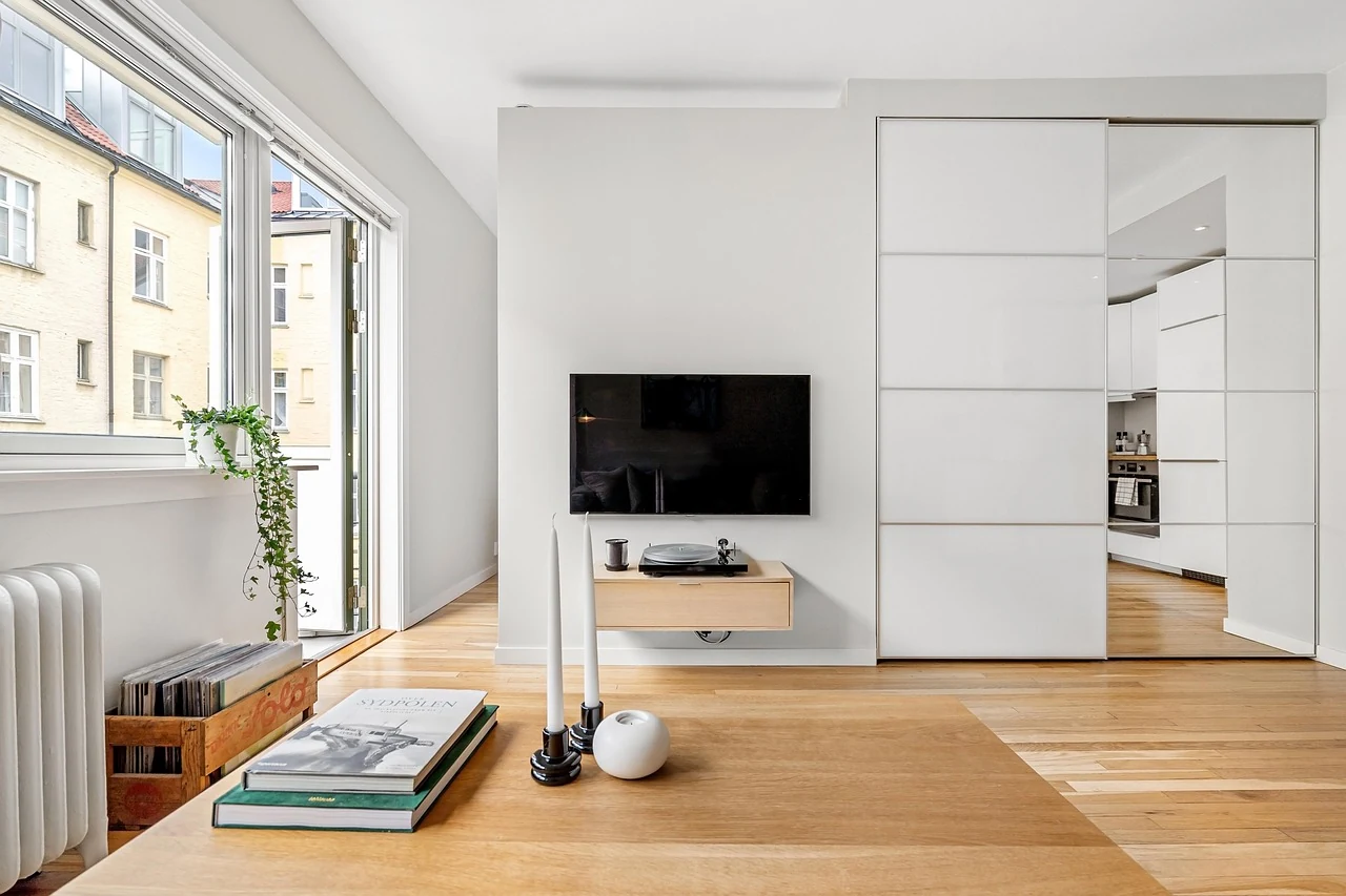 A wall-mounted television and low wood cabinet beside large windows