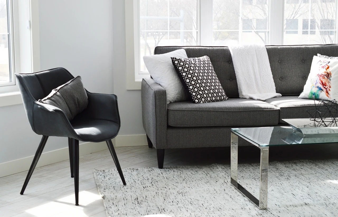 A dark chair and grey sofa beside broad living-room windows